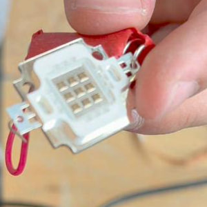 A hand holding the 10 W-class COB LED module: white ceramic body, a grid of emitter dies, metal solder tabs