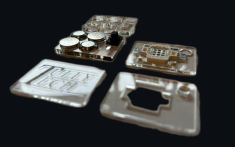 The V2 clear acrylic parts laid out at an angle: cells and switch plate, LED plate, cutout plates, engraved lid