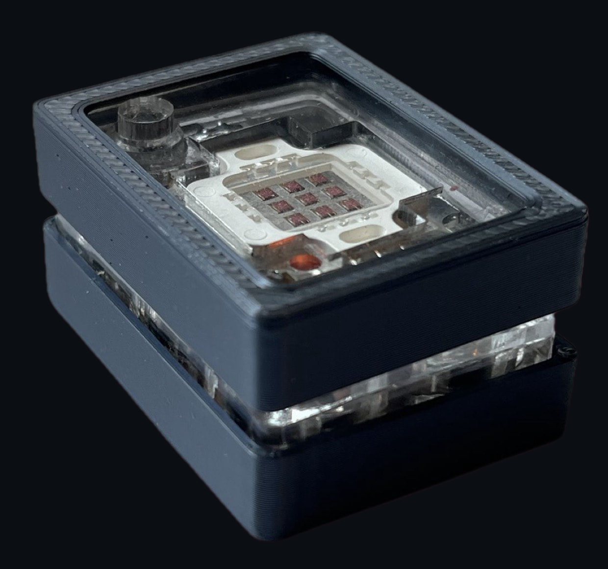 The final AntiCam pin, version 2: a dark grey case with a clear acrylic window over the emitter module and its three-by-three grid of emitters
