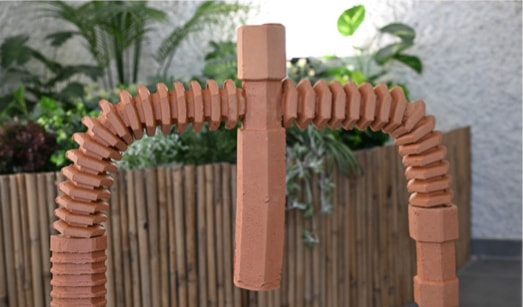 A ribbed terracotta clay arch standing in front of a bamboo fence and plants