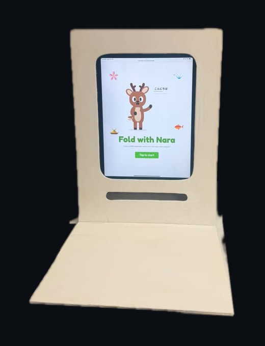 The booth’s iPad on its start screen: Nara, a cartoon deer, waves above the words “Fold with Nara” and a green “Tap to start” button
