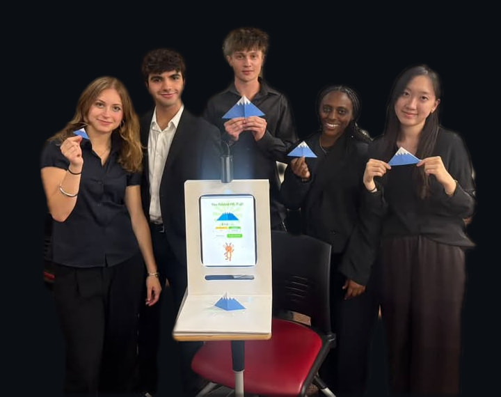 The five-person team at the demo in a USC classroom, each holding up a folded paper Mt. Fuji, with the booth in front of them