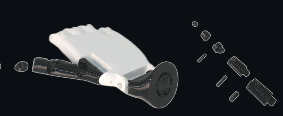 The physical arm exploded on a light gray tray: white printed palm and fingers, glossy black forearm and wrist collar, loose knuckle caps and pins